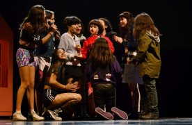 Foto de l'espectacle. Es veuen totes les adolescents actrius de l'obra al voltant d'una nina inflable vestida que estan manipulant