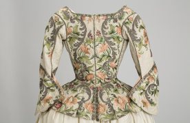 Vista trasera de una casaca femenina, s. XVIII, seda labrada, con aplicación de bordado que dibuja motivos florales polícromos.
