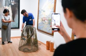 El guia del museu ensenya a una senyora com es pesca la sípia amb nanses. Un noi està retratant l'acció amb el seu mòbil.