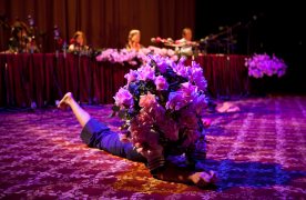 Fotografia de l'obra. Es veu una actriu estirada a terra amb una màscara feta de roses