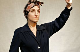 Dona amb bata de vestir i mocador al cap amb un puny alçat