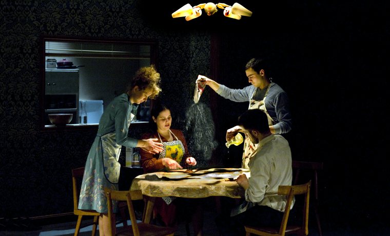 Quatre personatges, dos homes i dues dones, al voltant d'un taula cuinant