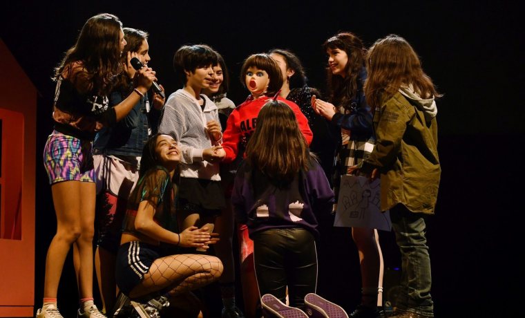 Foto de l'espectacle. Es veuen totes les adolescents actrius de l'obra al voltant d'una nina inflable vestida que estan manipulant