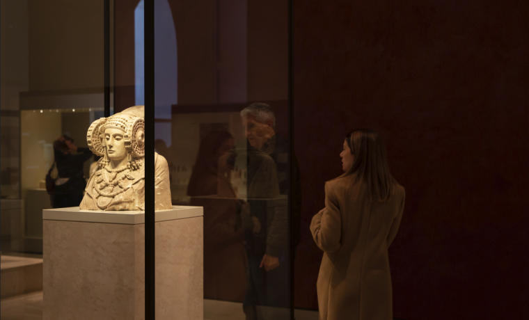 Dama de Elche en una vitrina y dos visitantes que la observan desde la izquierda