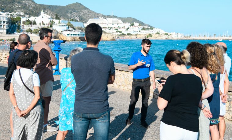 El guia està explicant a un grup de persones la costa marinera del Garraf. El grup es troba a l'exterior del museu abans de començar la visita a l'interior.