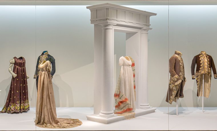 Imagen que muestra los distintos trajes y vestidos que se encuentran en la vitrina "Un nuevo clasicismo", que aborda la indumentaria de comienzos del siglo XIX. Forma parte del recorrido de la visita por la exposición permanente del Museo.